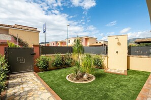Un barrio residencial con entrada pavimentada, césped cuidado y un pequeño jardín circular con una palmera.
