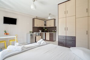 Habitación de hotel con cama, escritorio con silla, televisor, kitchenette y armario.