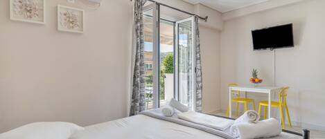 A hotel room with a bed, a desk with chairs, a TV, and a balcony with curtains.