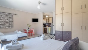 Een hotelkamer met twee bedden, een bureau, een stoel, een televisie en een kitchenette.