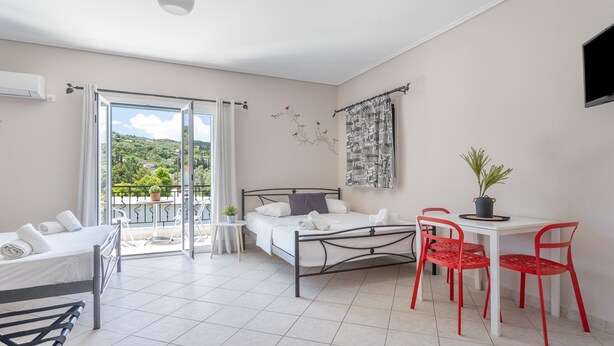 Een hotelkamer met een bed, een kleine tafel met stoelen, een balkon met uitzicht en een aan de muur bevestigde televisie.