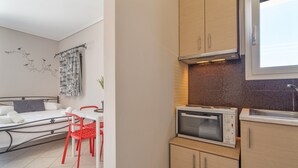 Een compacte kamer met een bed, een eettafel met rode stoelen, een kitchenette met een magnetron en een raam.