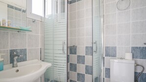 Et badeværelse med glasbrusekabine, vask og toilet.