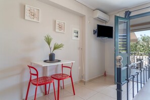 A balcony with a white table, two red chairs, a potted plant, and a TV mounted on the wall. - Apartment 'Alexandros Amea' with Mountain View, Wi-Fi and Air Conditioning (Lefkada Town)