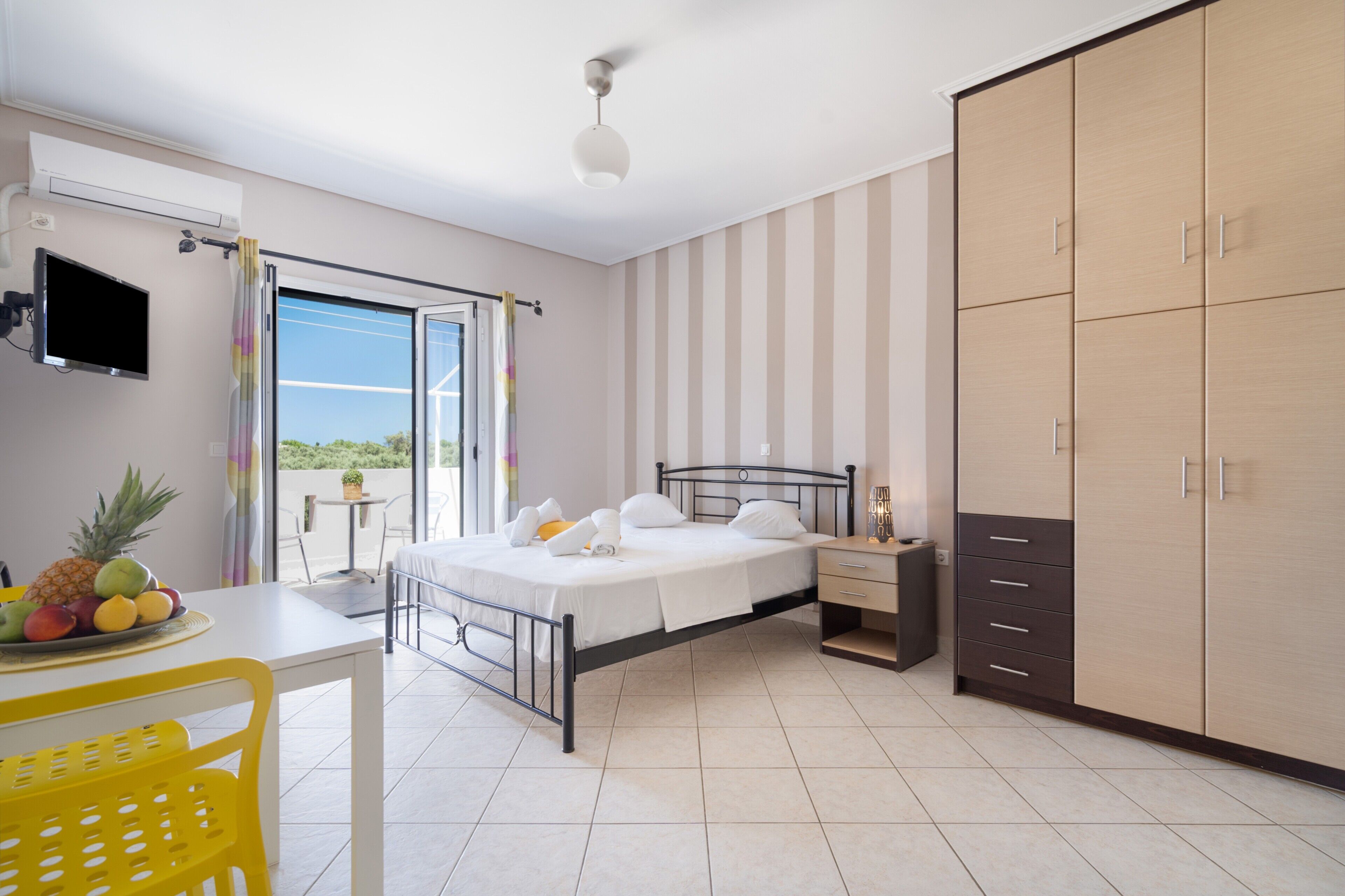 A bedroom with a bed, bedside table, wardrobe, and a view through a window.