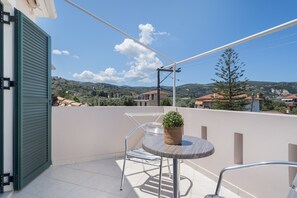 Een balkon met een tafel, een stoel, een plant in pot en uitzicht op huizen en heuvels.