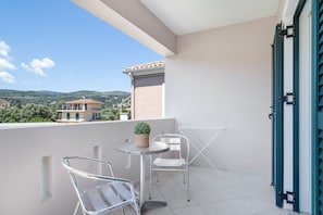 A balcony with a table and two chairs, a potted plant, and a view of a building and landscape.