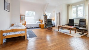 A room with two wooden beds, a rocking chair, a wooden table, and a large window.
