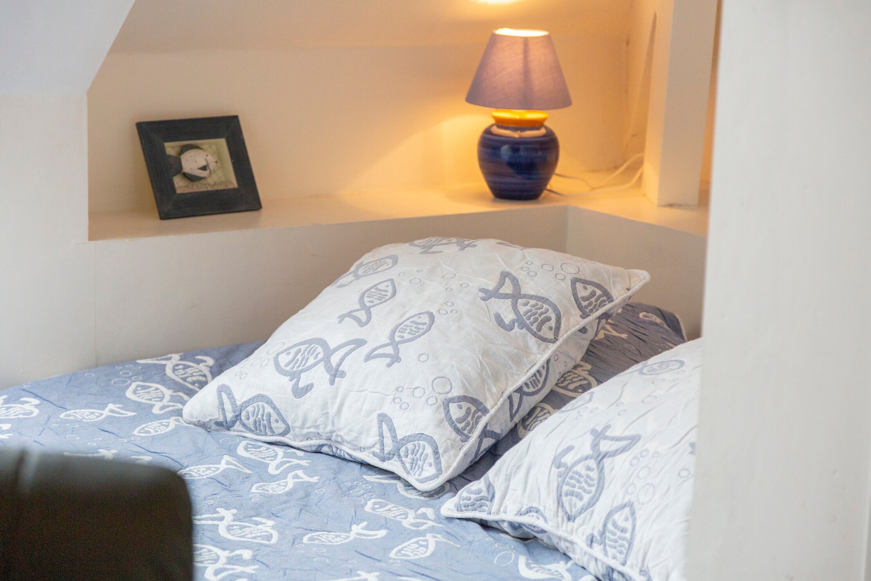 Une chambre à coucher avec un lit, des oreillers, une lampe et un tableau encadré accroché au mur.
