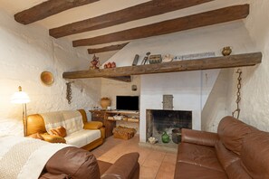 A rustic living room with exposed wooden beams, a fireplace, leather sofas, and a television.