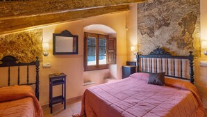 A bedroom with two beds, a stone wall, wooden beams, a window with shutters, and a small table. - Country House 'Emilli' with Mountain View, Wi-Fi and Air Conditioning (Unknown)