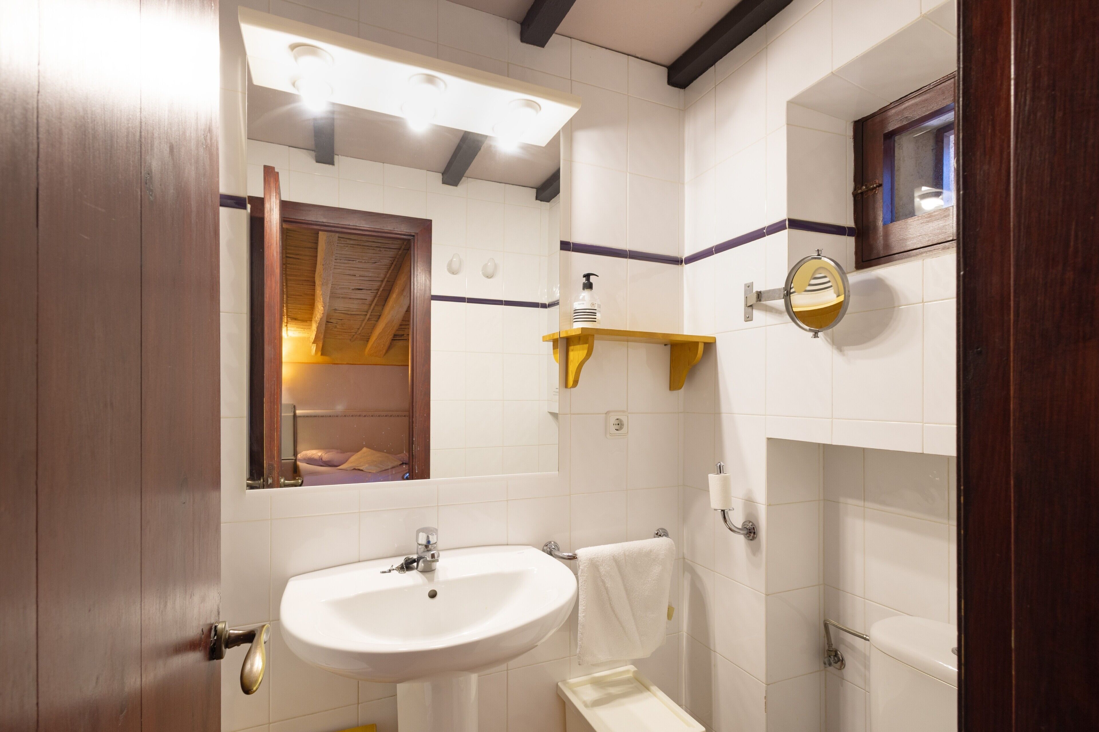 Un baño con lavamanos, espejo, toallero y puerta de madera.