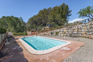 A rectangular swimming pool with a stone wall and trees in the background.