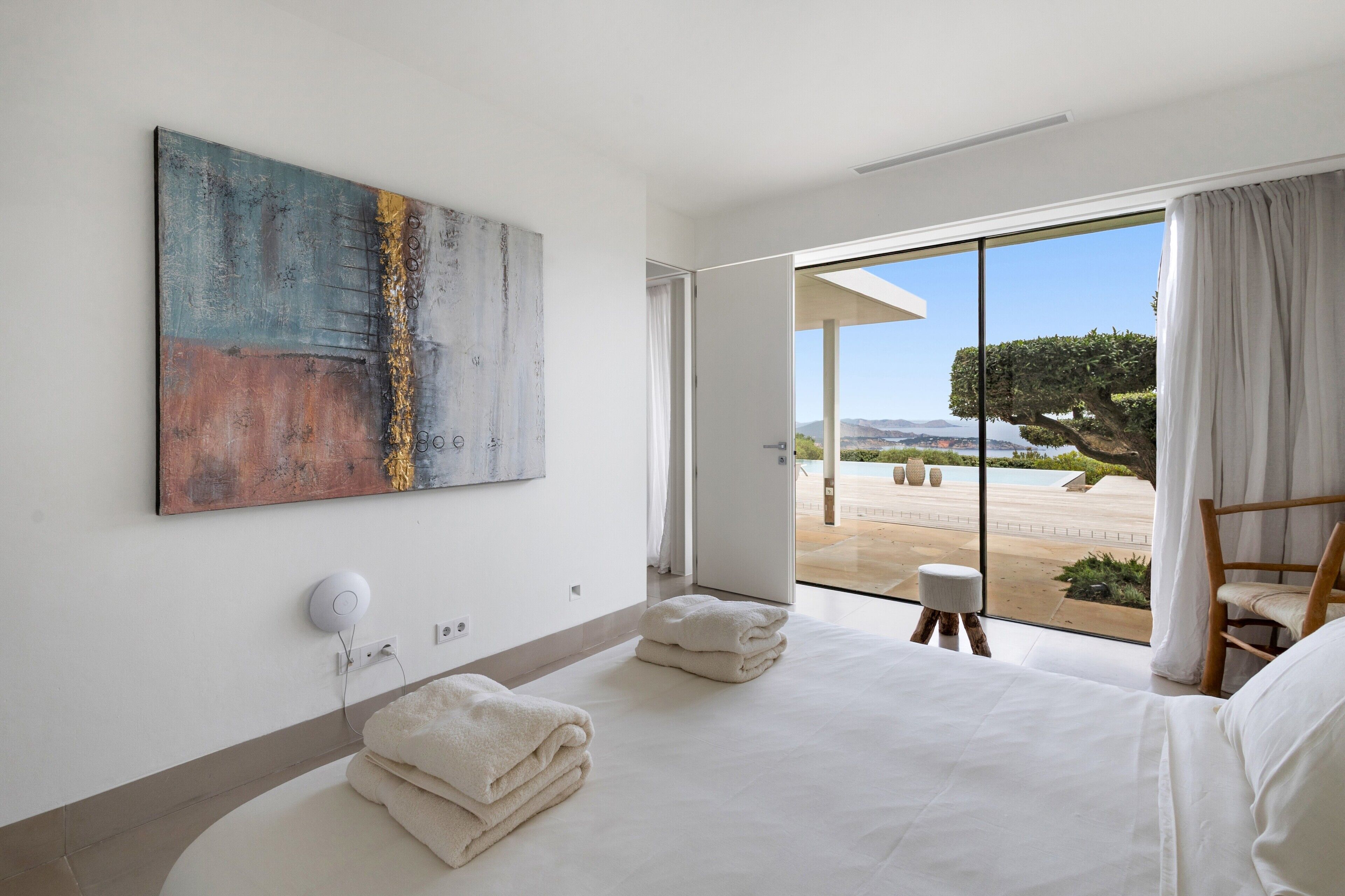 A modern hotel room with a large bed, a painting on the wall, and a view of the outdoors.