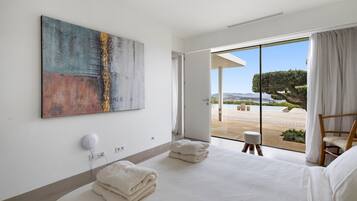 A modern hotel room with a large bed, a painting on the wall, and a view of the outdoors.