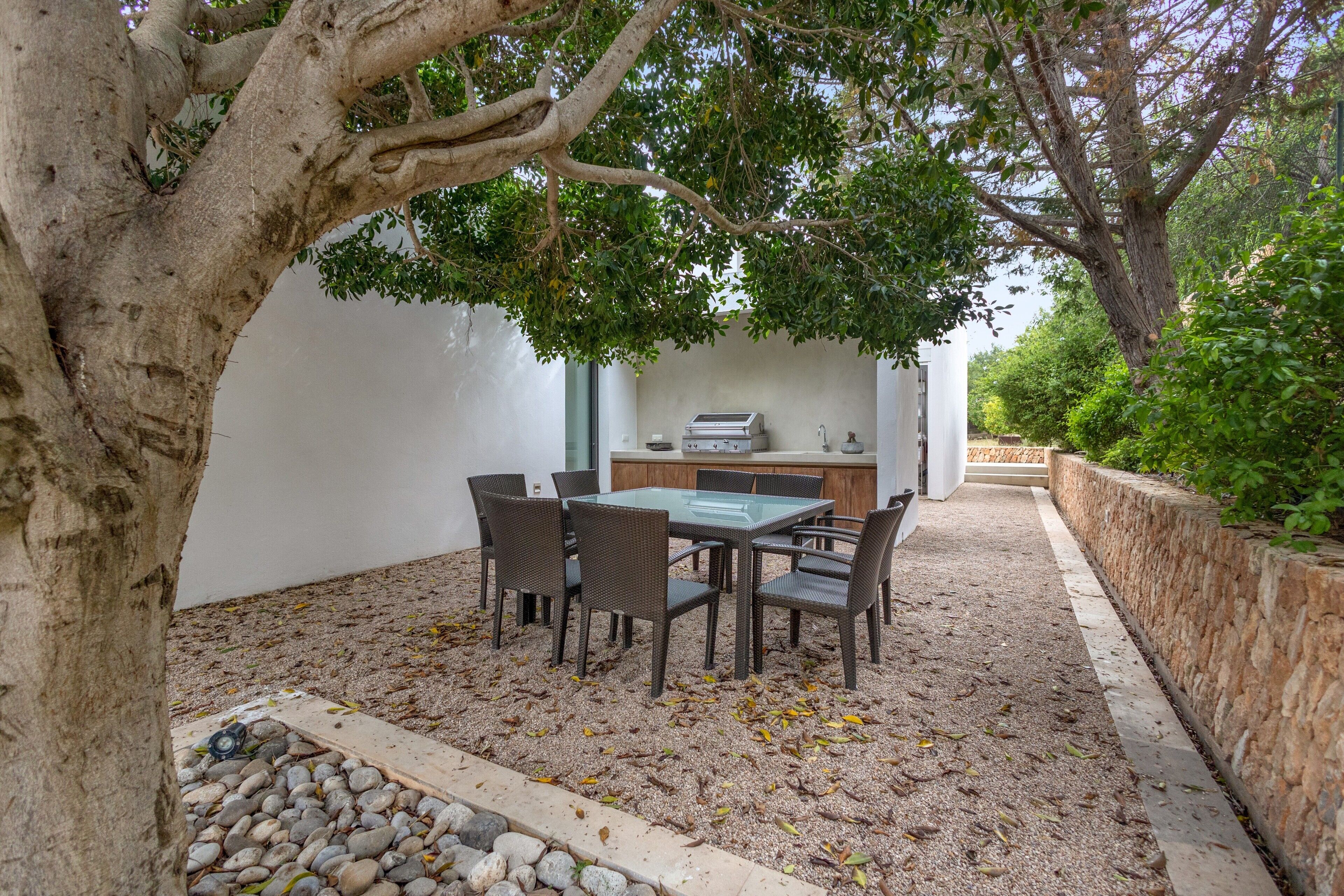 An outdoor dining area with a table and chairs, surrounded by a stone wall and a tree.