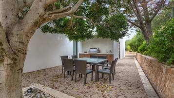 An outdoor dining area with a table and chairs, surrounded by a stone wall and a tree.