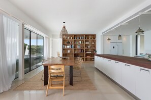 A modern kitchen with a wooden island, a dining area with chairs, and a large bookshelf.