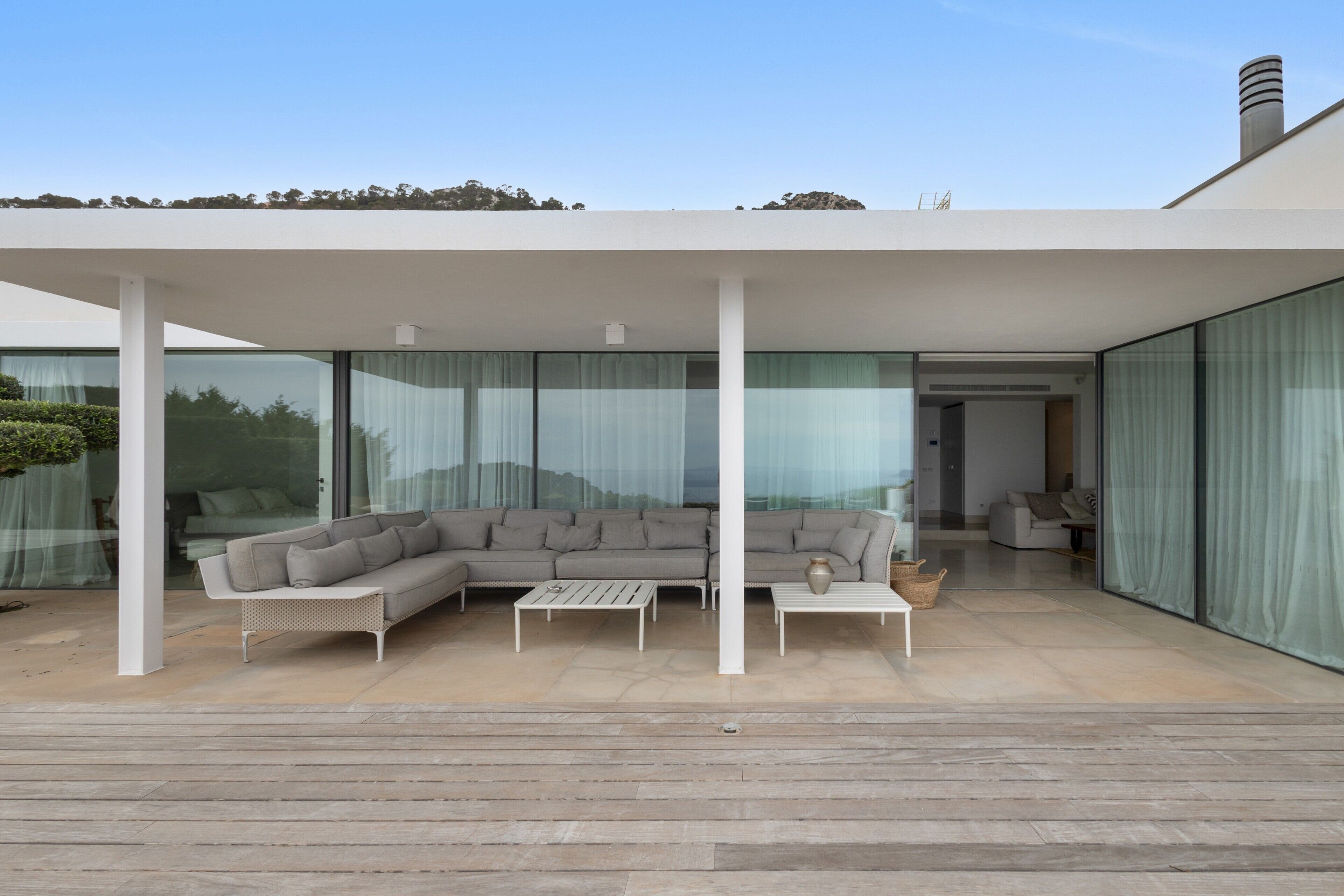 Un espacio exterior moderno con un sofá modular, dos mesas de centro blancas y una estructura de pérgola.