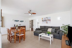 Una sala de estar con una mesa de comedor, sillas, un sofá, una mesa baja, un televisor y un ventilador de techo.