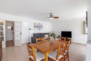 Un comedor con mesa y sillas de madera, televisor, sofá y ventilador de techo.