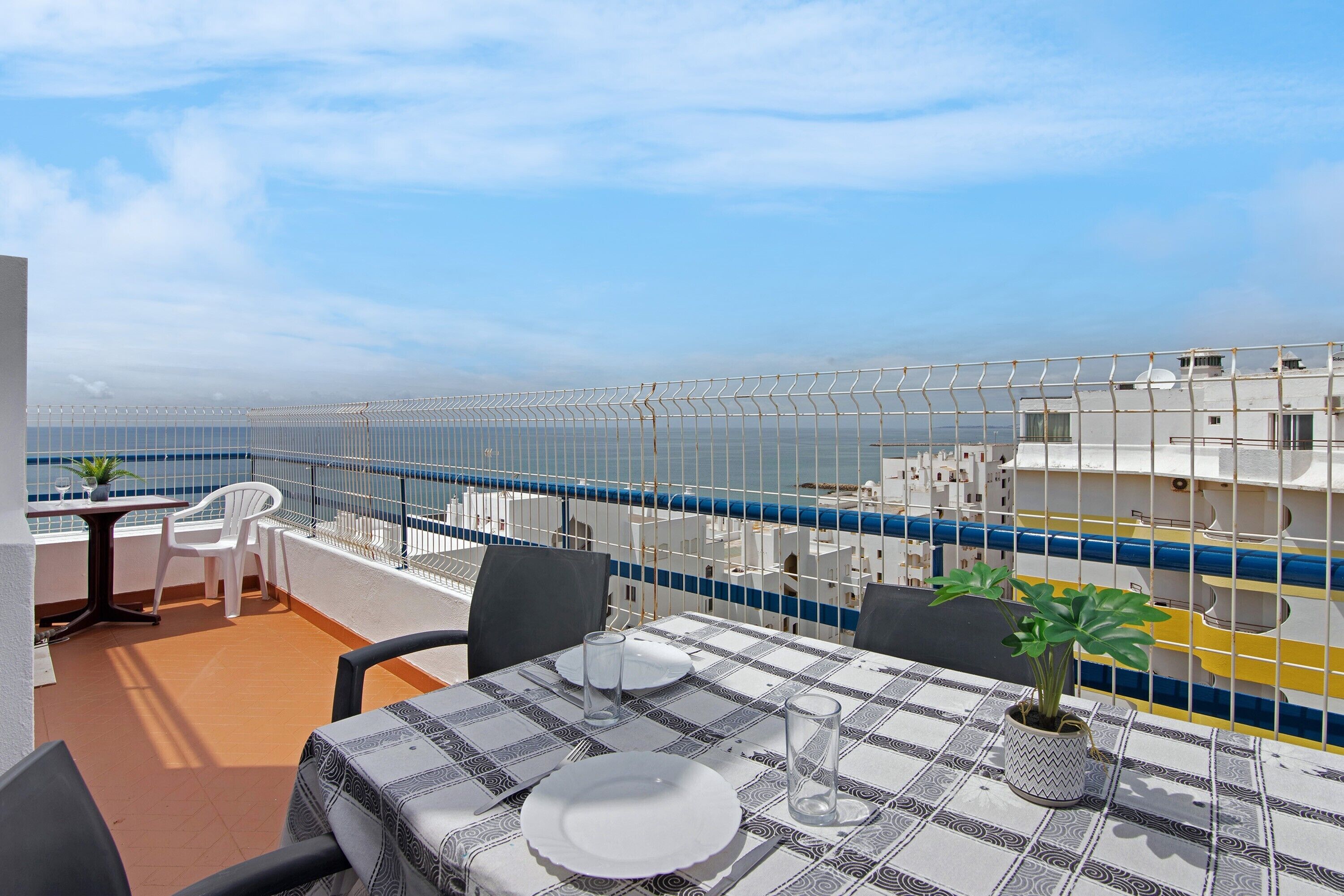 Een terras met een tafel voor twee personen, stoelen, een plant in pot en uitzicht op zee.