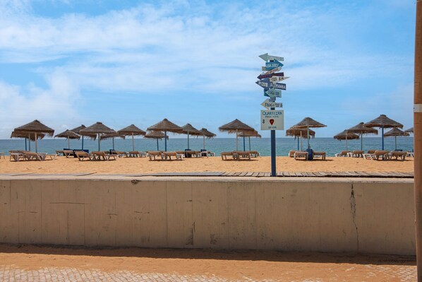Una playa con tumbonas y sombrillas, un cartel con indicaciones y vista al mar.