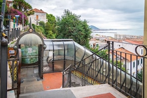 A staircase with a glass enclosure leading to a terrace with a view of the city and sea.