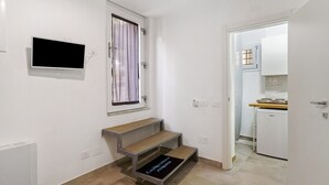 A room with a TV mounted on the wall, a window with curtains, a built-in bench, and a door leading to a kitchen area. - Apartment 'CasaMia Civico14 - Turchese' with Wi-Fi and Air Conditioning (Salerno)