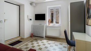 A room with a door, a radiator, a television, a window, a desk, and a chair.