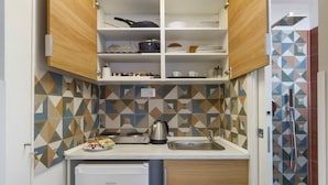 A compact kitchen with a built-in dishwasher, a kettle, and a sink.