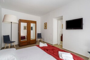 A hotel room with a bed, a red rug, a mirror, a wardrobe, a TV, and a lamp.