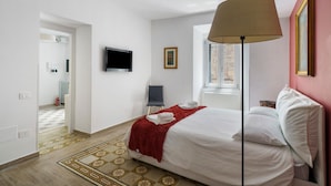 A hotel room with a bed, a TV, a window, and a red throw blanket.