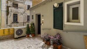Une cour avec un bâtiment, une porte verte, une fenêtre et des plantes en pot.