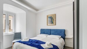 Un lit bien fait, avec une literie blanche et bleue, une tête de lit bleue et un tableau accroché au mur.