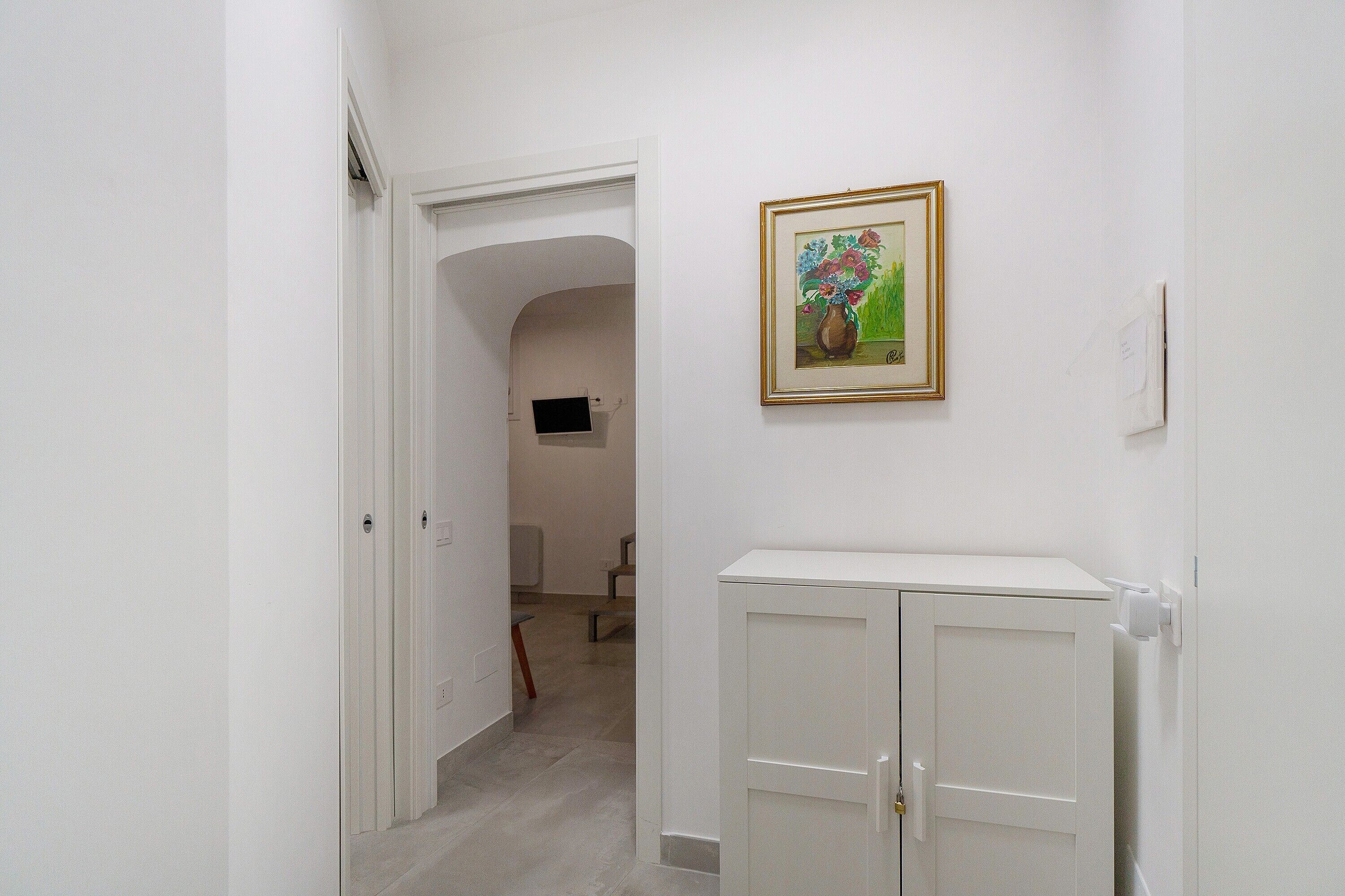 Ein Flur mit einer weißen Tür, einem weißen Schrank und einem gerahmten Gemälde an der Wand.