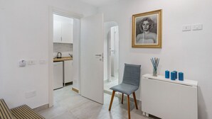 Un salon moderne avec un canapé blanc, un fauteuil bleu, une petite table avec des bougies et un tableau encadré au mur.