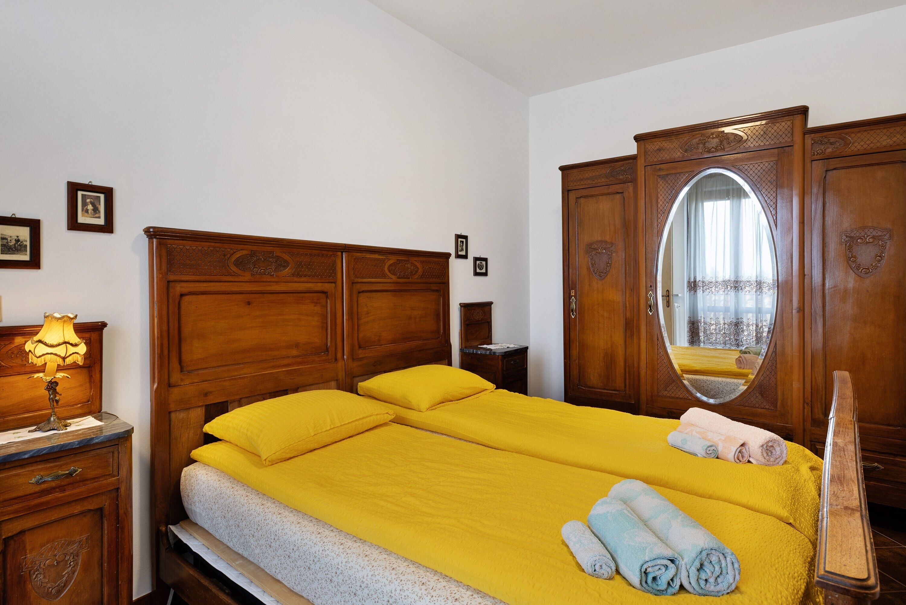 A double bed with a wooden headboard, a nightstand with a lamp, a mirror, and a wardrobe.