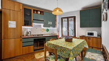 Une cuisine de taille réduite avec des meubles en bois, une table à manger recouverte d’une nappe à motifs floraux et un four à micro-ondes posé sur un plan de travail.