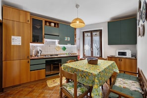 A compact kitchen with wooden cabinets, a dining table with a floral tablecloth, and a microwave on a counter.