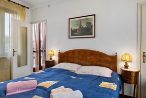 Une chambre à coucher avec une tête de lit en bois, un lit recouvert d’une courtepointe bleue, deux lampes de chevet, un tableau accroché au mur et une porte dotée d’un panneau de verre.