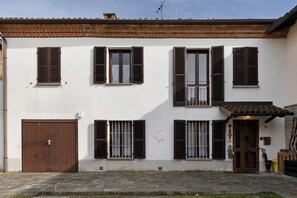 Un bâtiment à deux étages avec une façade blanche, de nombreuses fenêtres dotées de volets, une porte marron et un petit porche.