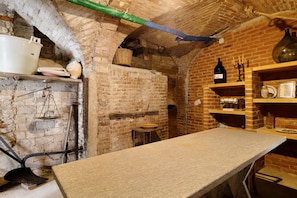 A rustic kitchen with a brick wall, a stone countertop, and shelves with various kitchen items.