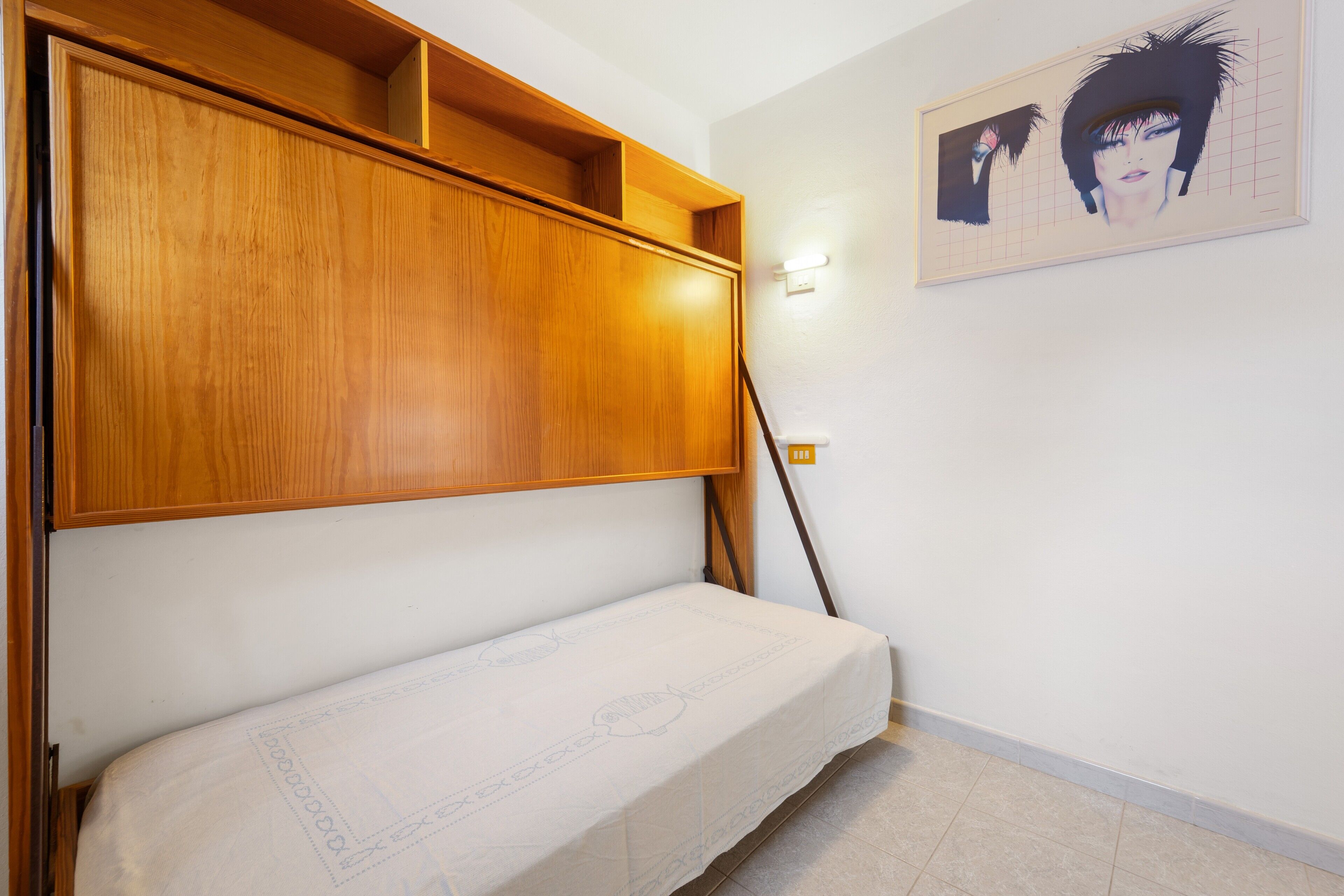 A room with a wooden bed frame, a wall-mounted shelf, and a framed artwork.