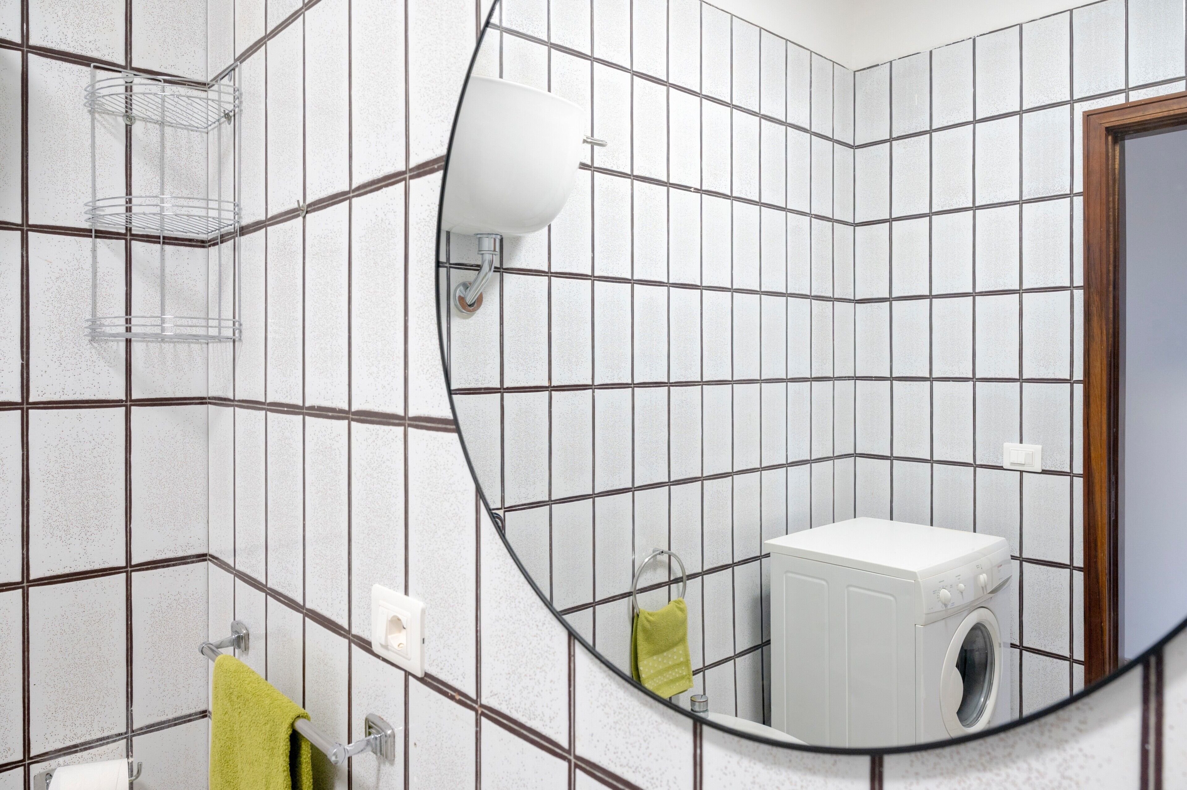 Ein Badezimmer mit Fliesen, einem Waschbecken, einem Spiegel, einem Handtuchhalter und einer Waschmaschine.