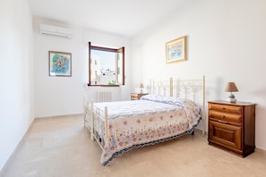 Een slaapkamer met een bed, een houten nachtkastje, een raam en een radiator.