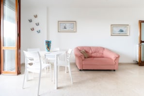 Een kamer met een roze bank, witte stoelen, een tafel en vlinderstickers op de muur.