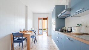 A modern kitchen with a dining area, featuring a wooden table and chairs, a blue cabinet, and a patterned floor. - Apartment 'Stella' with Sea View, Wi-Fi and Air Conditioning (Otranto)
