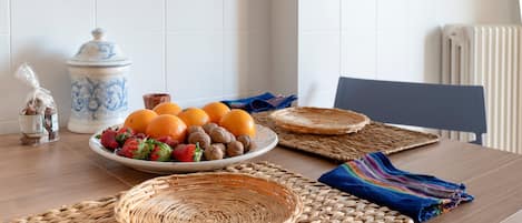 A dining table with a plate of fruit, a ceramic jar, and woven placemats.