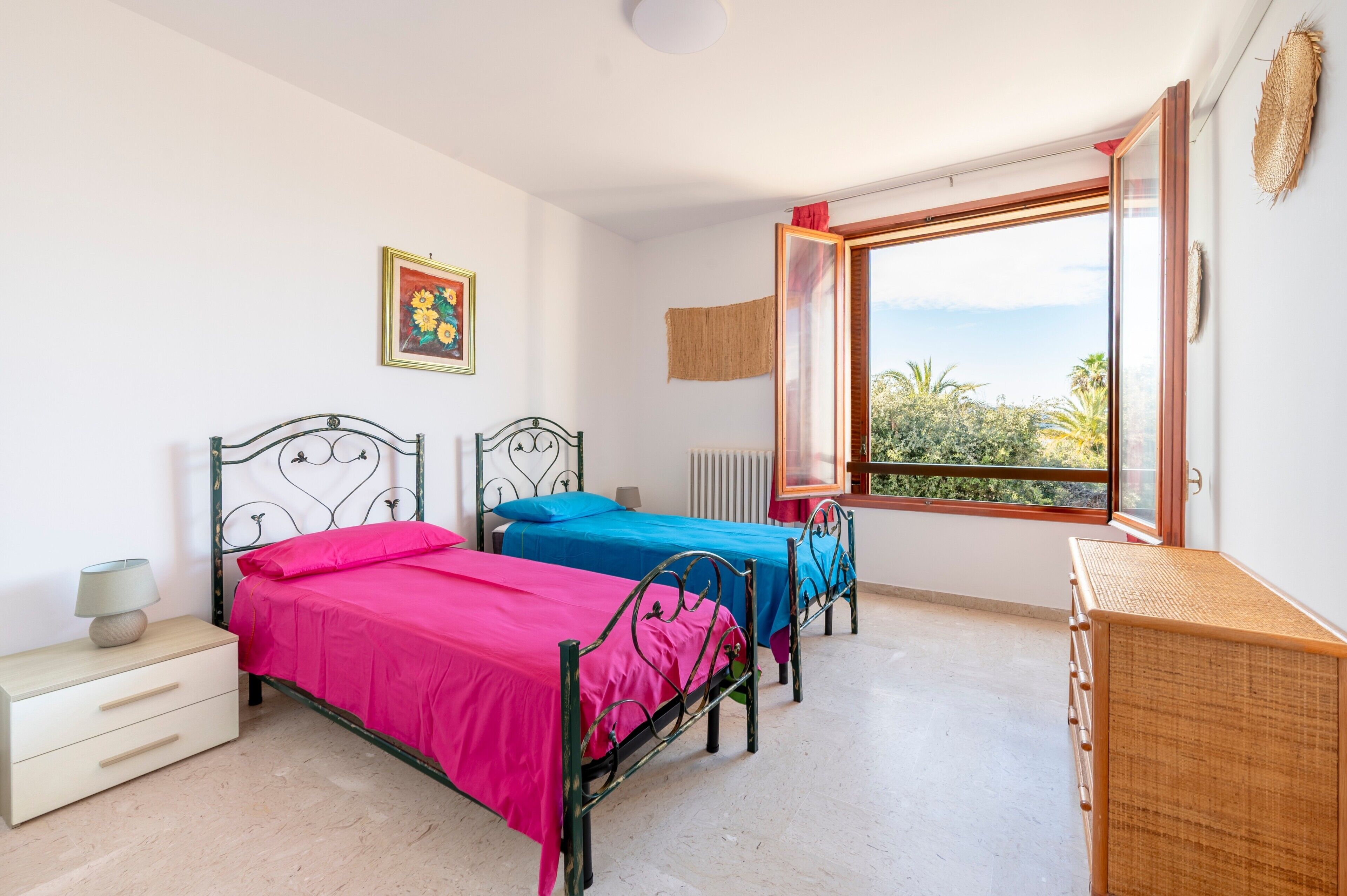 A bedroom with two beds, a dresser, a radiator, and a window with a view.